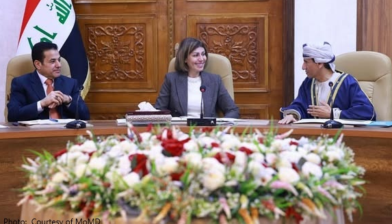 A person sitting at a table with a person in a suit

Description automatically generated