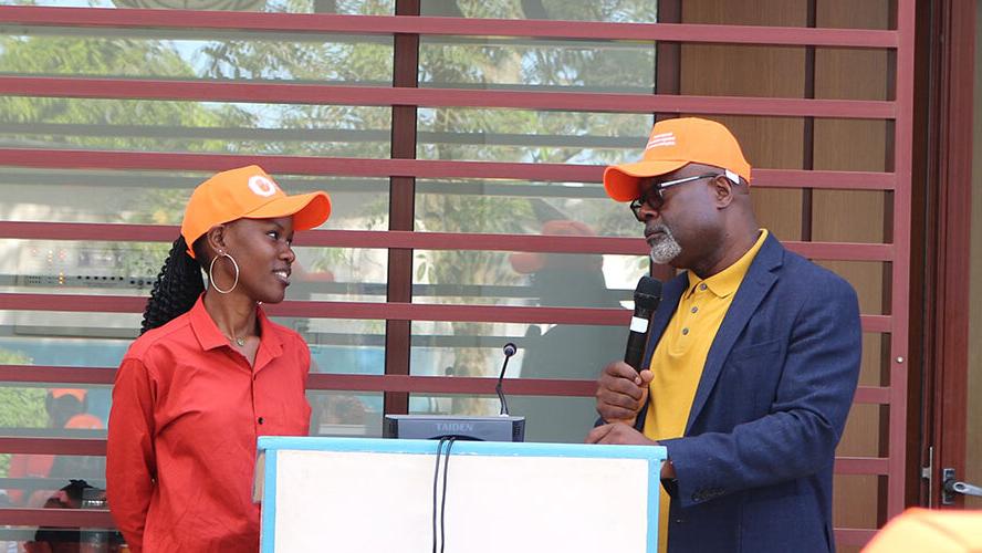 A young woman in an orange baseball cap smiling and speaking to a man also wearing an orange baseball cap. 