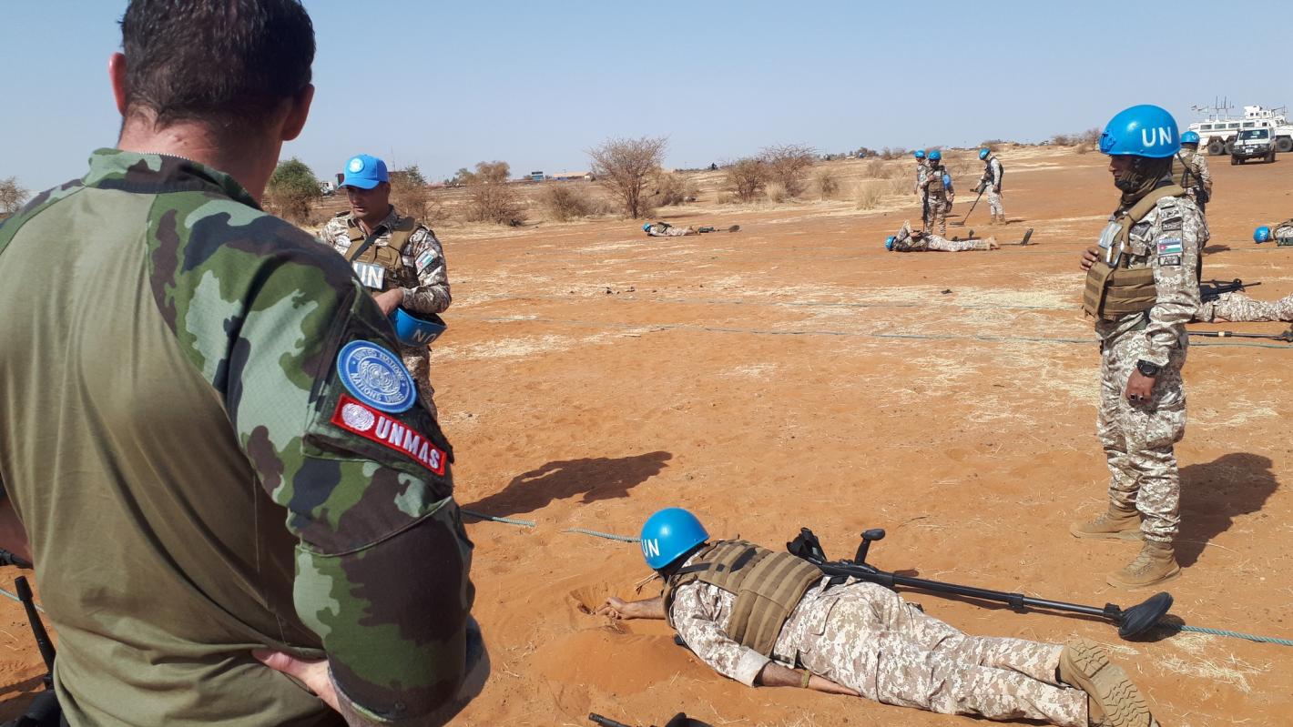 UN peacekeepers conduct a controlled mine detection training exercise in a desert environment under UNMAS supervision.
