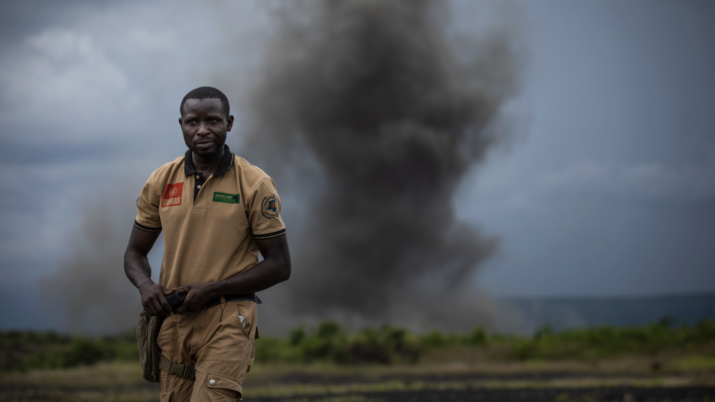 a man is standing in a field with smoke behind him.