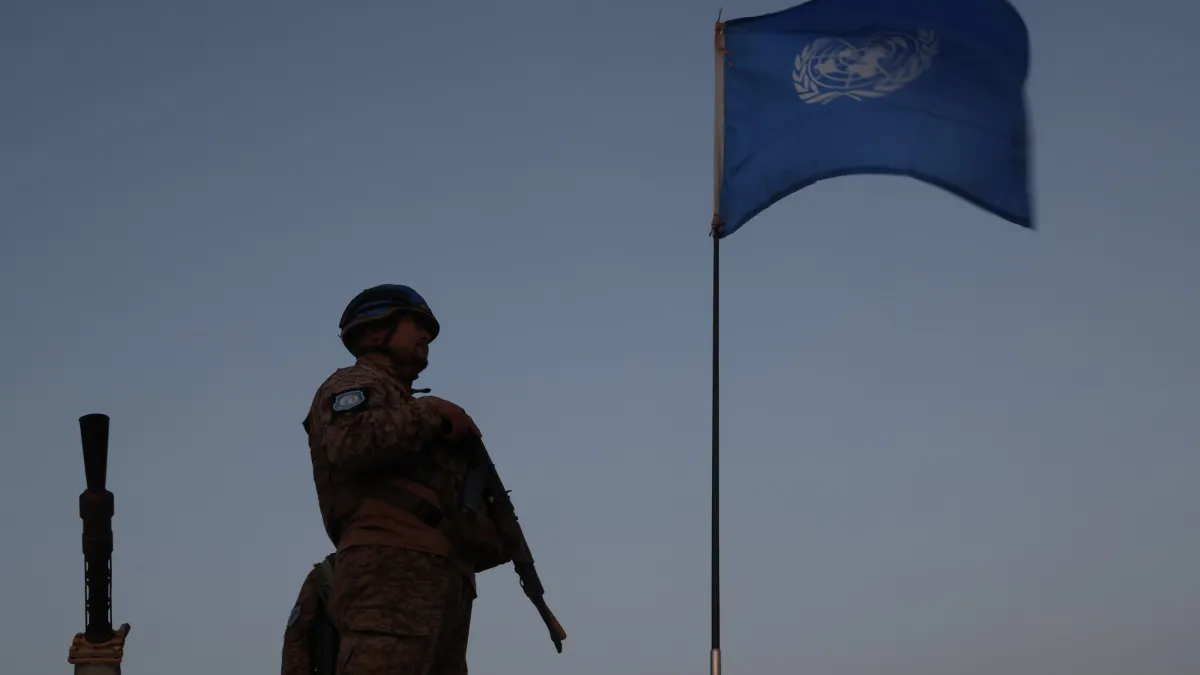 A UN peacekeeper standing next to the UN flag