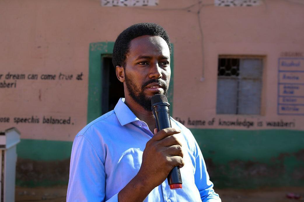 Mohamed Sheikh Said Haji speaks with a microphone in front of a school