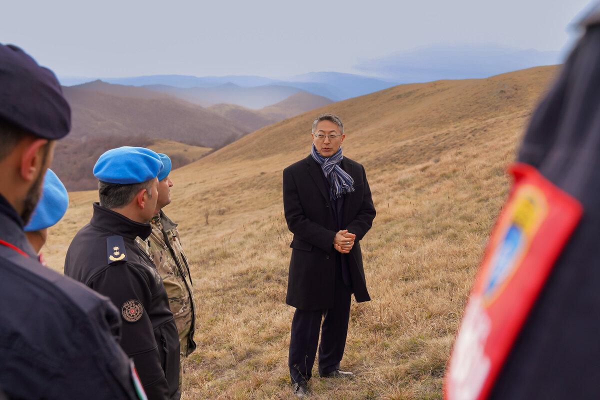 Deputy Special Representative of the Secretary-General and OiC UNMIK Milbert Dongjoon Shin led a delegation of peacekeepers to the site of the 1999 plane crash to pay tribute to the victims. peacekeepers standing in field for rememberance event