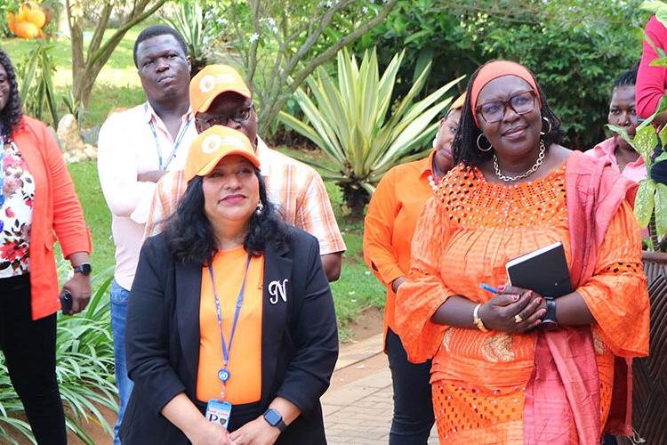 A group of people standing together and smiling watching what is happening on a stage which is not pictured.