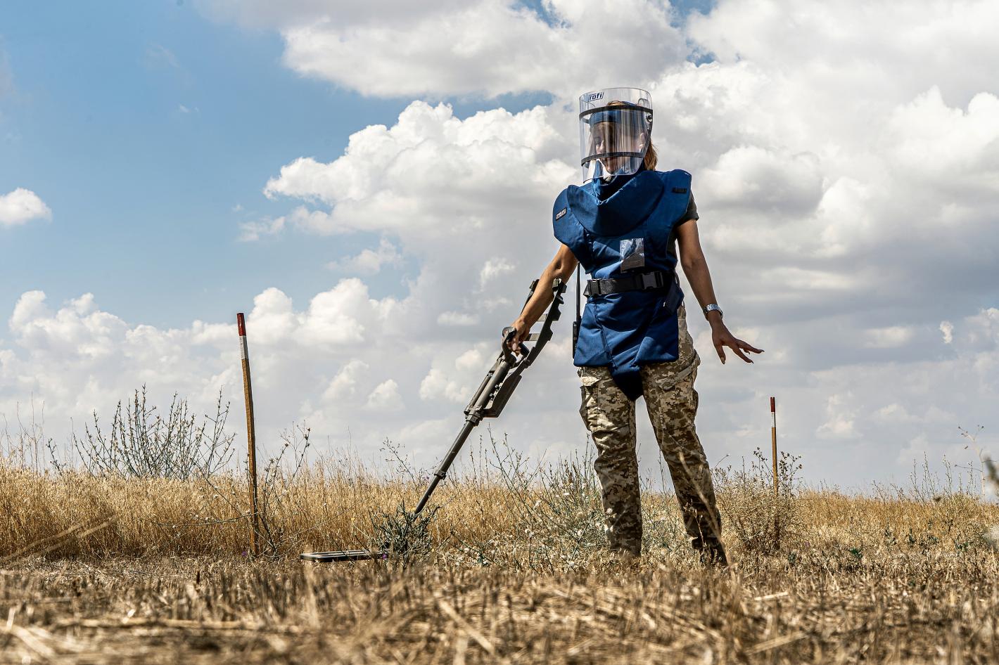 a female deminer is clearing the land with a detector