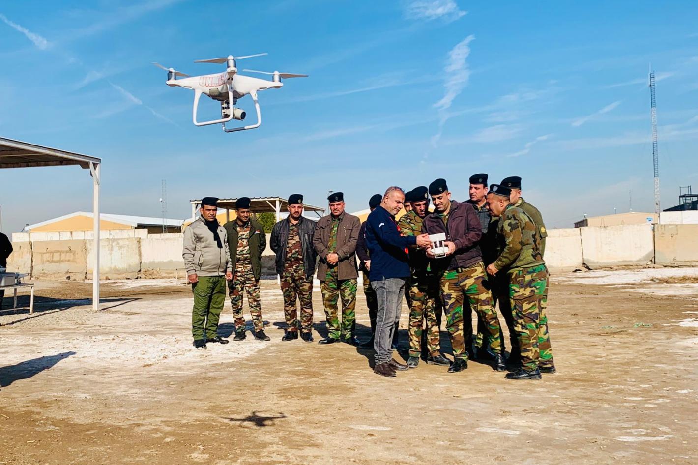 some men with uniforms are getting trained with a drone flying in front of them