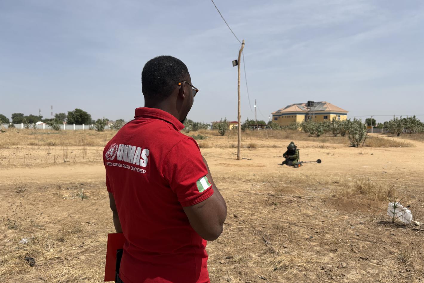 a man with UNMAS shirt overlooking a deminer