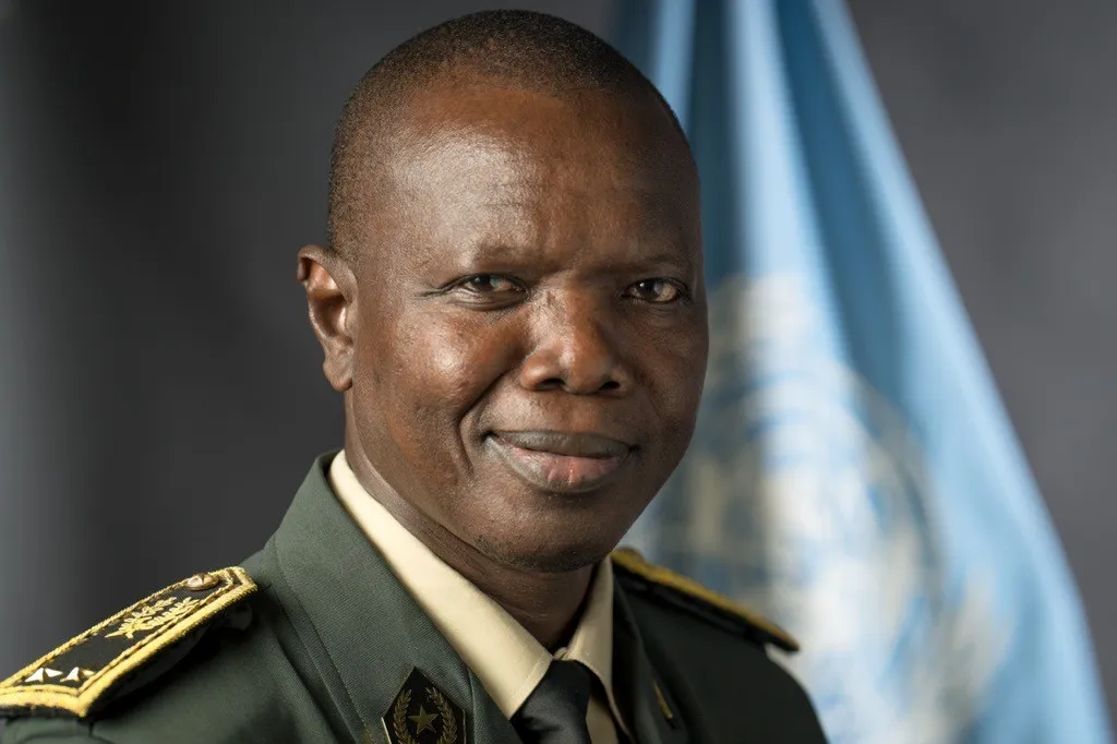 Man in uniform smiling with UN Flag in background