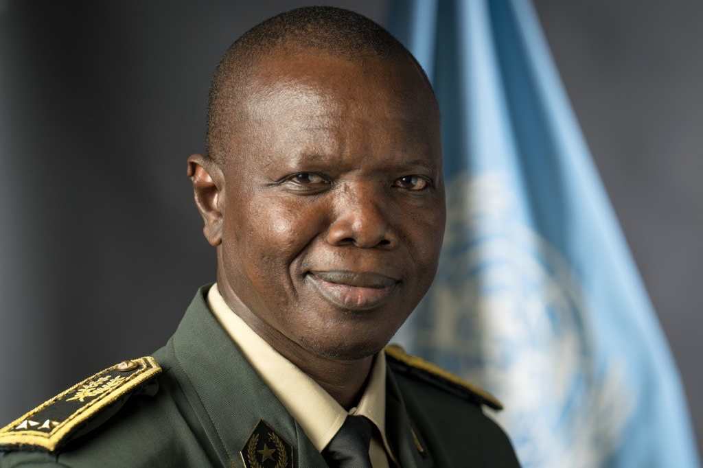 Man in uniform smiling with UN Flag in background