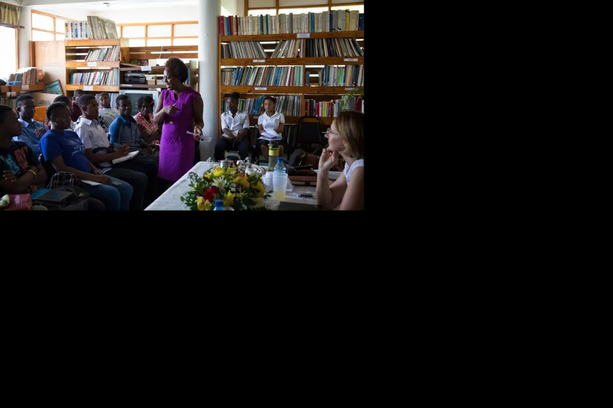 A group of people sitting in a library listening to a woman in a purple dress speaking to the group.