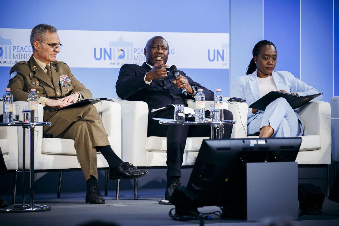 A man addressing the audience seated with two other members of a panel.