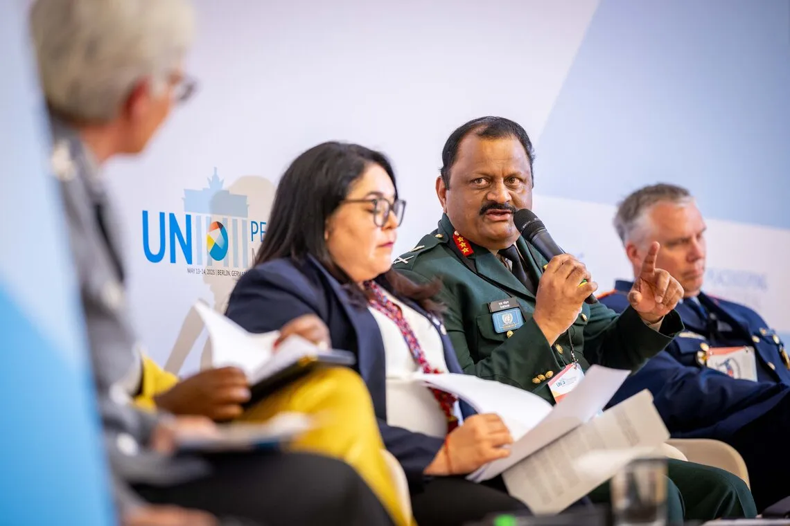 two men and two women panelists on a stage. A man in a military uniform is holding a microphone.