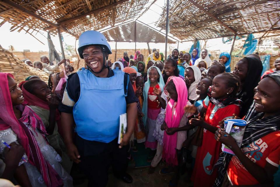 A female peacekeeper stands smiling in the middle of crowd of civilians