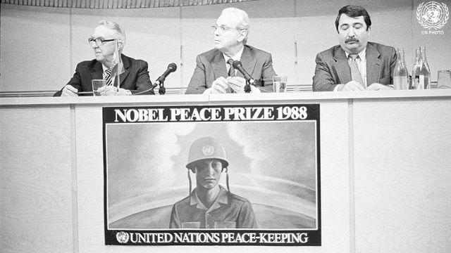 A black-and-white photo of three men behind a podium, above a poster that reads Nobel Peace Prize 1988, United Nations Peace-keeping