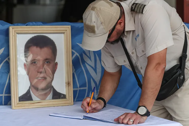 A peacekeeper signing a condolence book next to a photo of a fallen peacekeeper