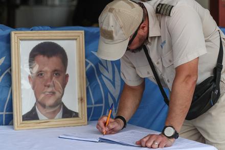 A peacekeeper signing a condolence book next to a photo of a fallen peacekeeper